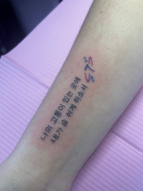 Close-up of an arm with Korean characters tattooed vertically on the forearm against a pink background