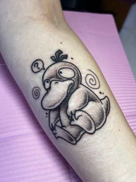 Black and gray tattoo of a whimsical character with bulbous features and a crown, adorned with spiral designs on the arm