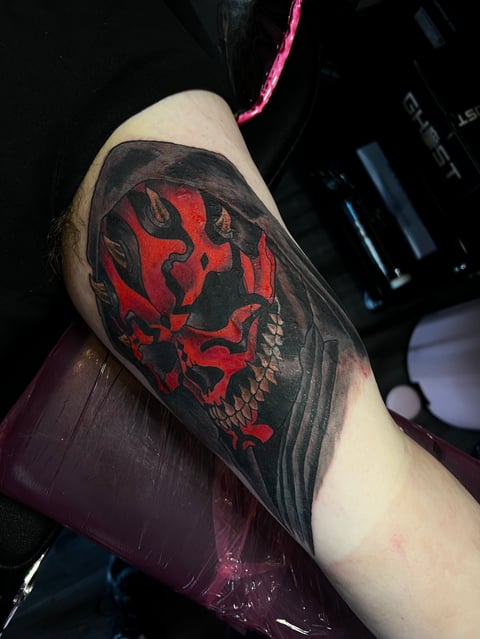 Tattoo of red and black Darth Maul face design on persons upper arm