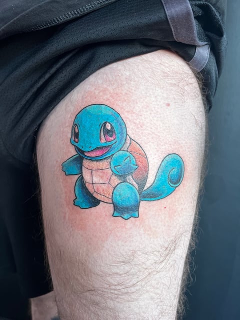 Blue and tan Squirtle Pokemon tattoo on persons thigh, showing the turtle character with closed eyes and happy expression