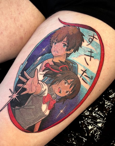 Anime-style tattoo on arm featuring two characters with brown hair in an oval frame with purple and red border and sparkles