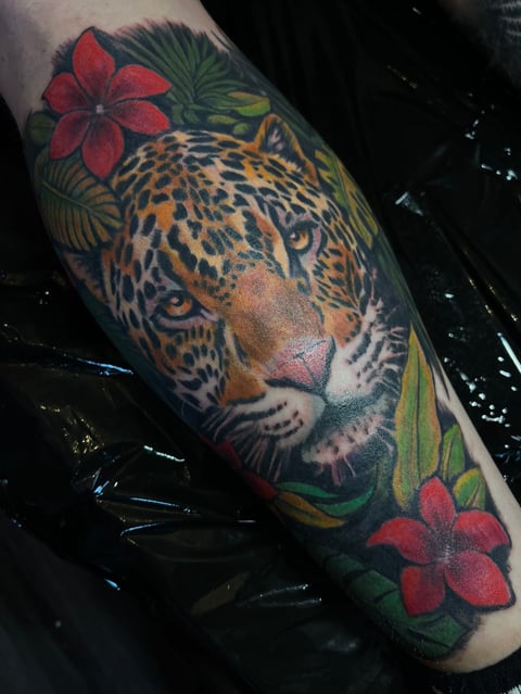 Colorful leopard tattoo on arm with red flowers and green foliage surrounding the animals detailed face