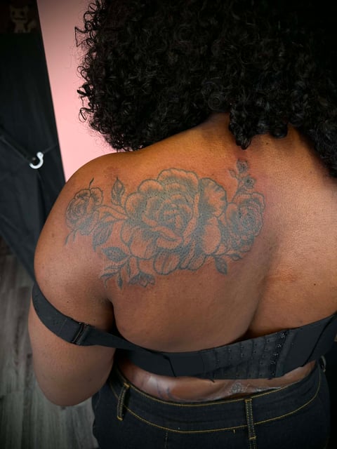 Person from behind showing a large rose tattoo on upper back and shoulder with gray ink