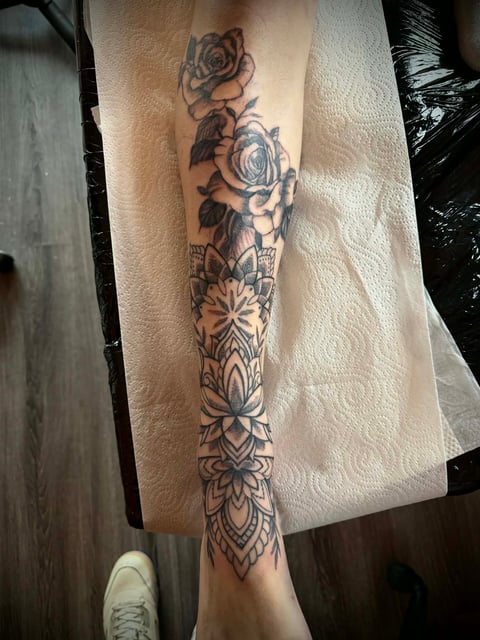 Full leg tattoo sleeve featuring roses, mandalas, and geometric floral patterns in black ink on a person's leg