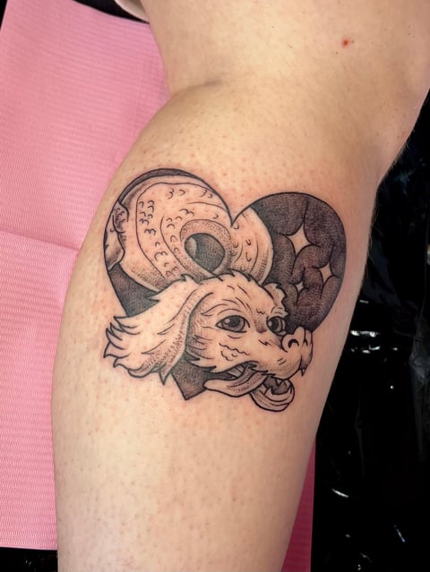 Black ink tattoo on forearm of a ram head with crescent moons and celestial design elements