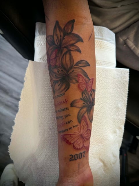 Forearm tattoo featuring purple and pink flowers with text and the year 2007, wrapped with a white bandage