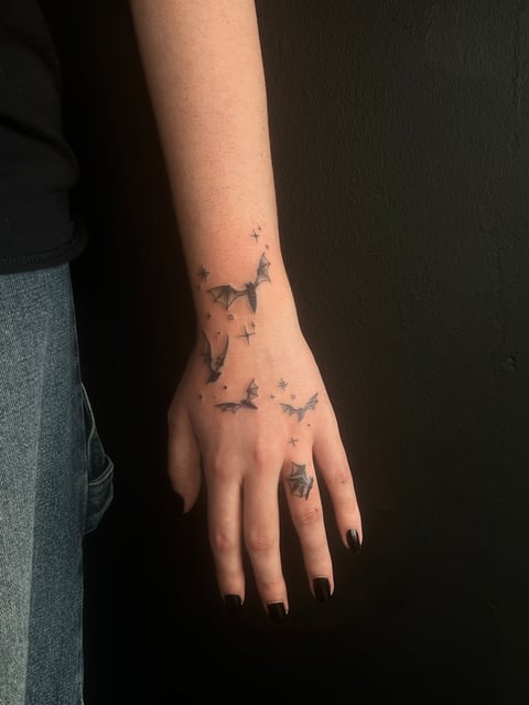 Close-up of a hand and forearm with bird tattoos and small stars scattered across the skin
