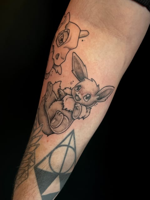Arm tattoo featuring cartoon characters including a cute mouse-like creature holding an acorn and other playful figures in black ink