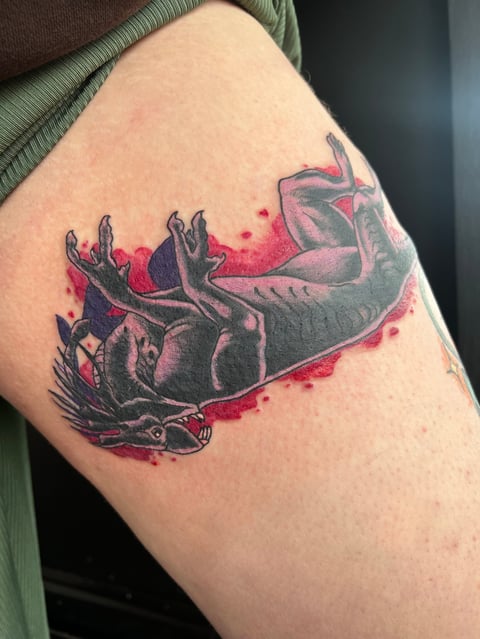 Tattoo of a black and red axolotl with pink watercolor splashes on someones upper arm or shoulder